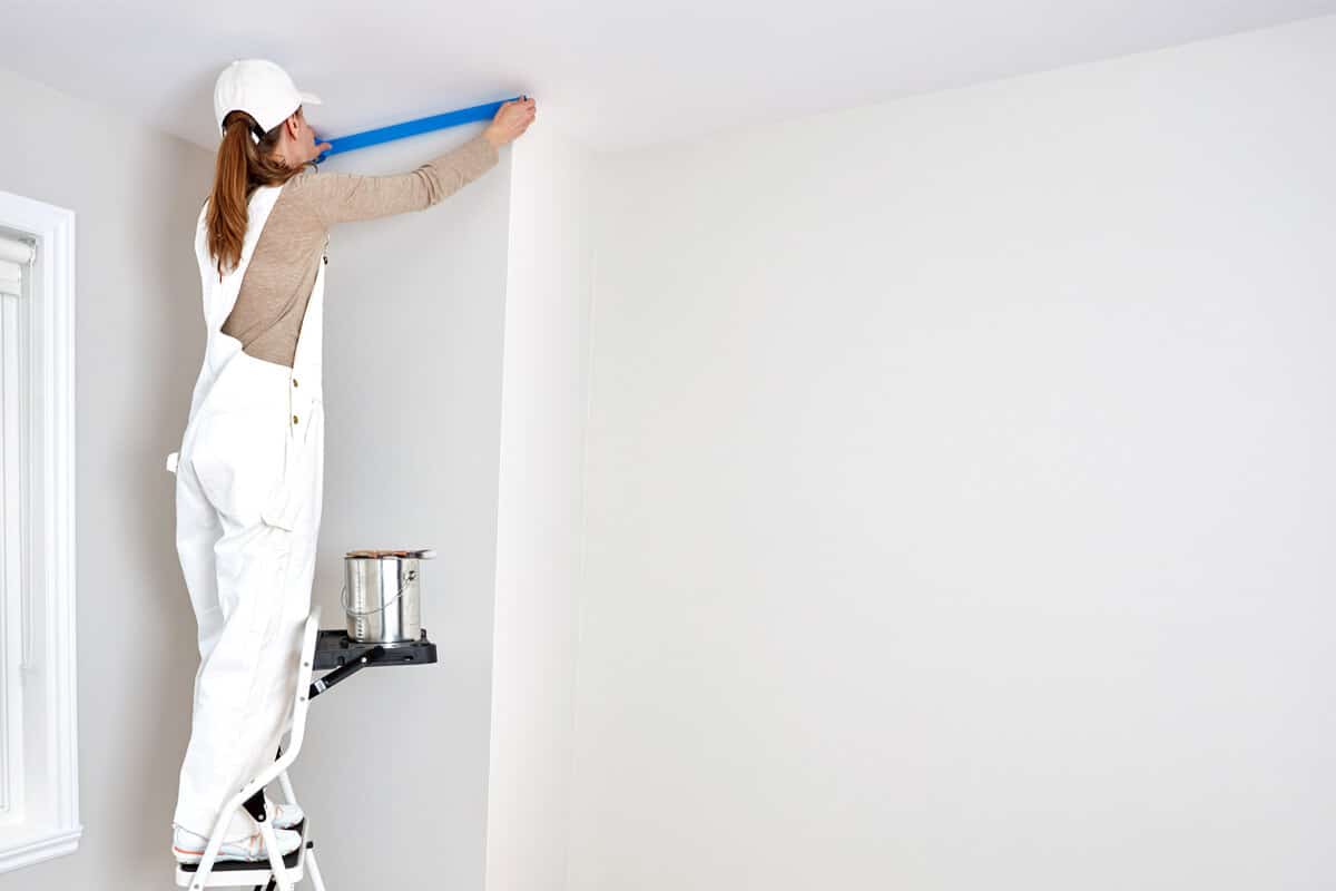 Painter applying masking tape along the wall to create a clean edge before painting the ceiling.