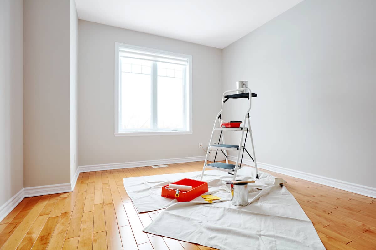 Painting equipment, including brushes, rollers, and paint trays, set up in an interior room ready for painting.